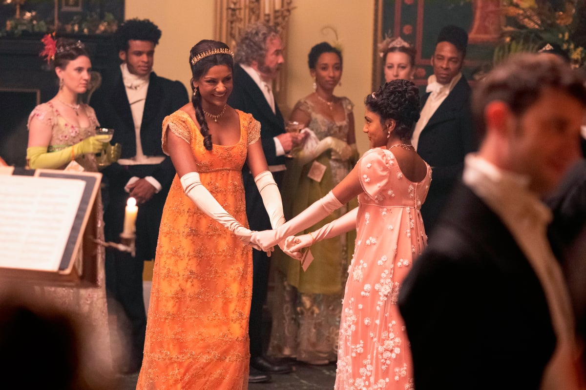 Simone Ashley as Kate Sharma, Charithra Chandran as Edwina Sharma in Bridgerton Season 2. The sisters laugh at a ball.