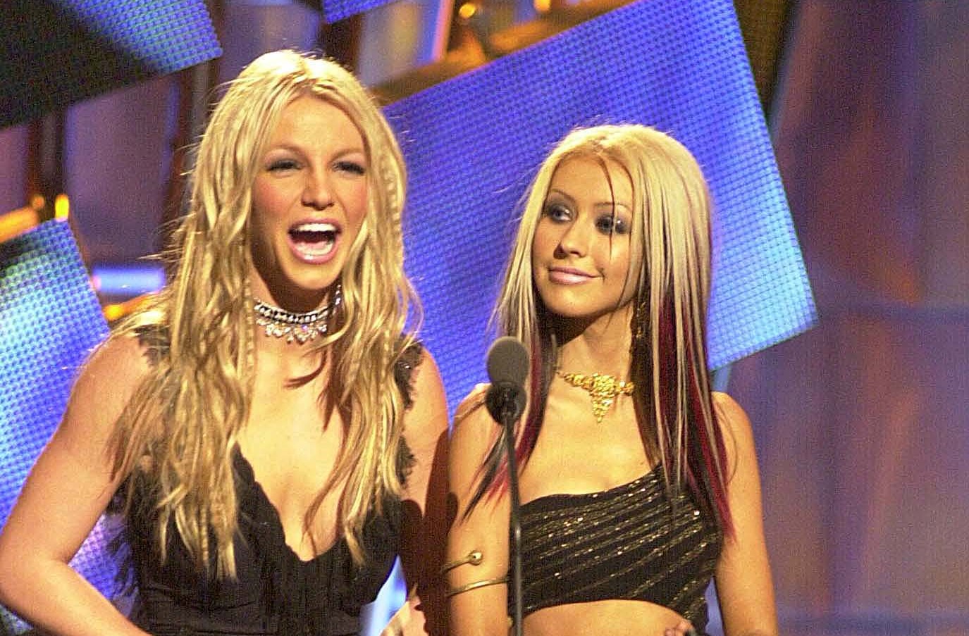 Britney Spears and Christina Aguilera wear black tank tops and stand in front of a microphone at the VMAs.