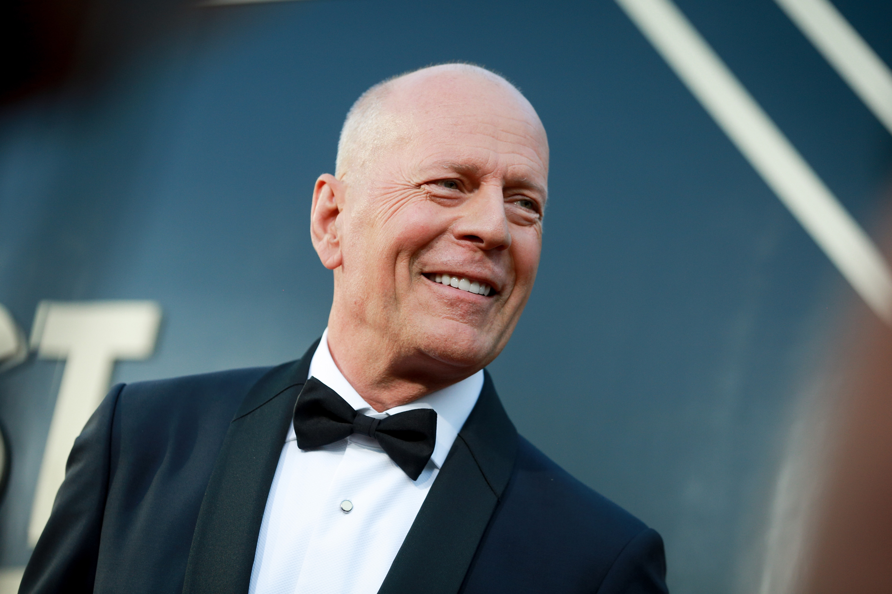 Bruce Willis wears a tuxedo and smiles.