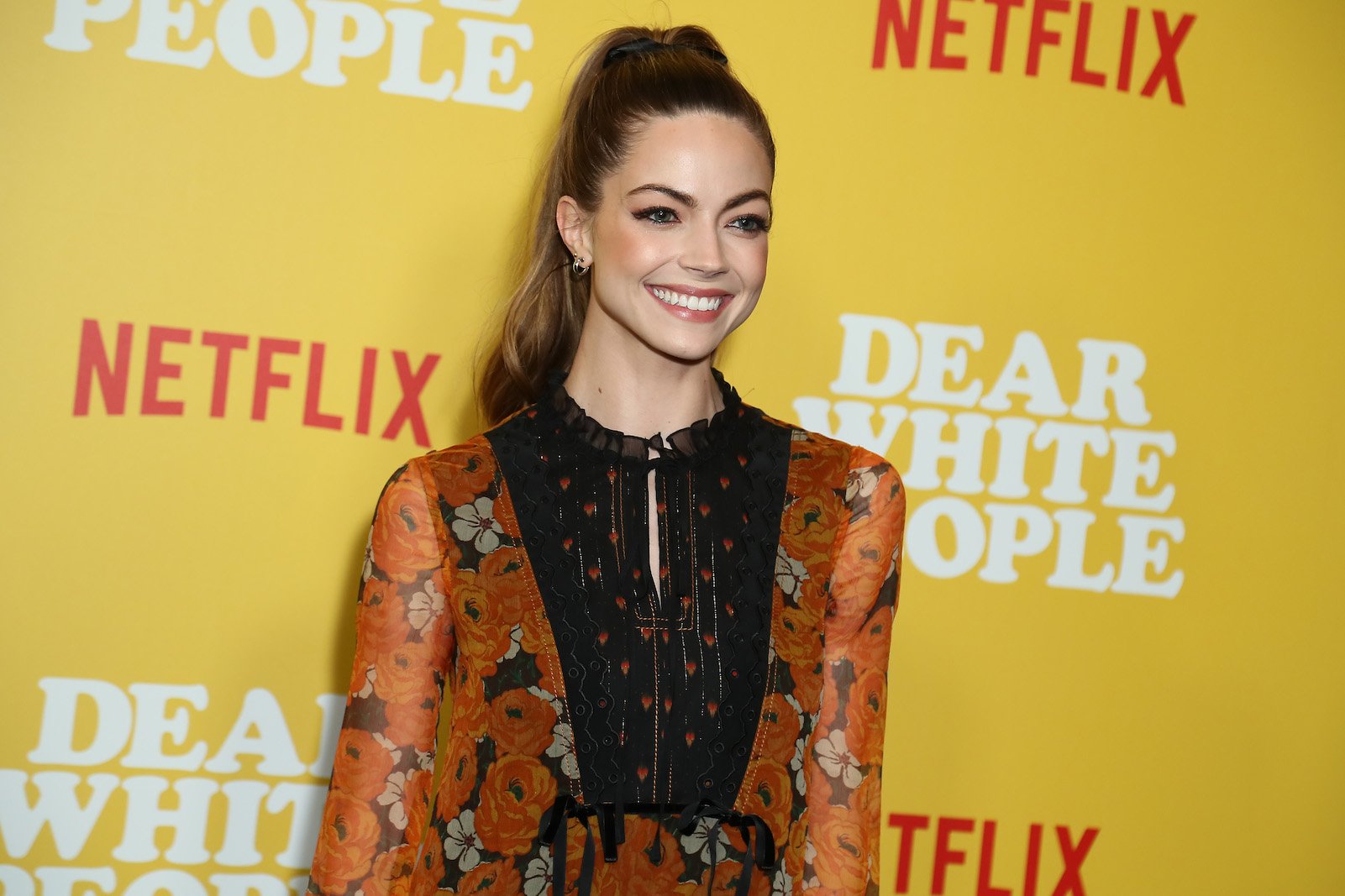 New 'Chicago Fire' Season 10 cast member Caitlin Carver smiling at an event against a yellow background 
