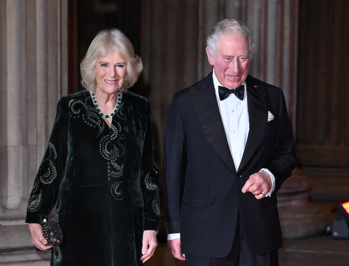 Camilla Parker Bowles smiles wearing a green dress as she walks next to Prince Charles in a tuxedo