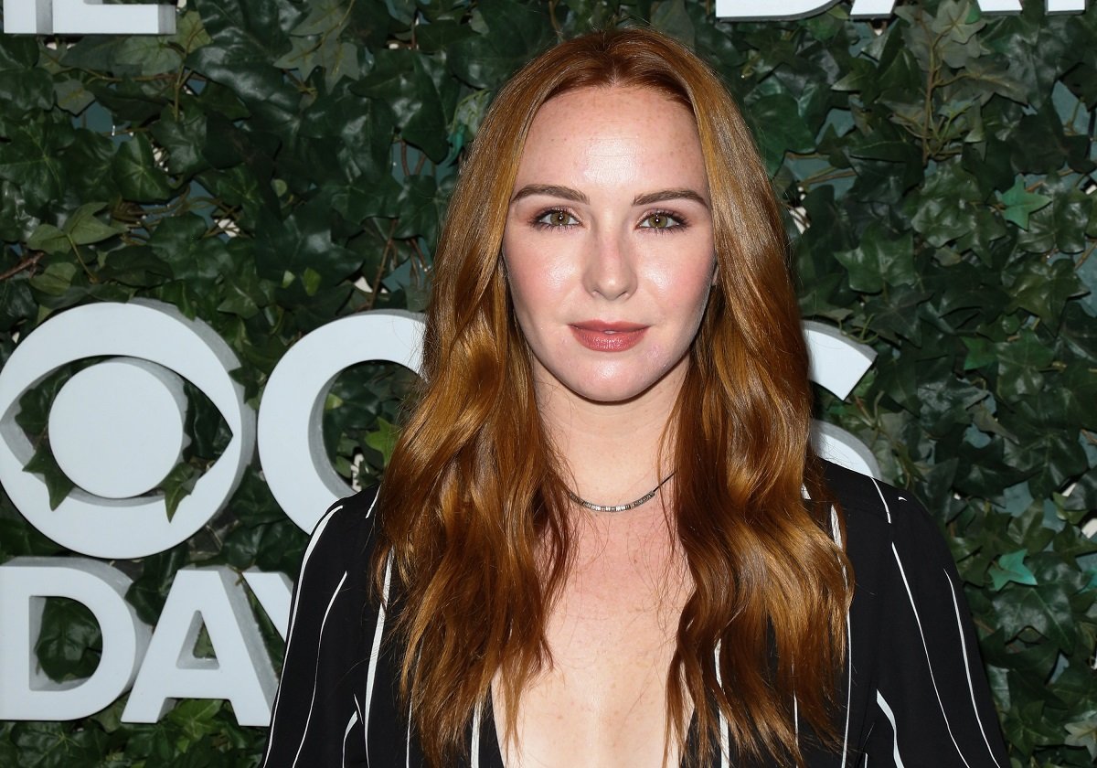 'The Young and the Restless' actor Camryn Grimes wearing a black and white striped jumpsuit, and standing in front of a hedge.