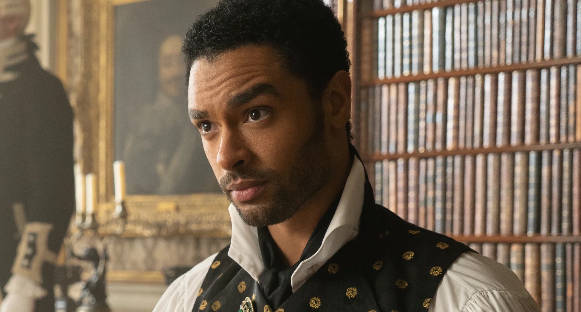 Character Simon Basset from 'Bridgerton' in relation to Season 2 wearing vest in home library.