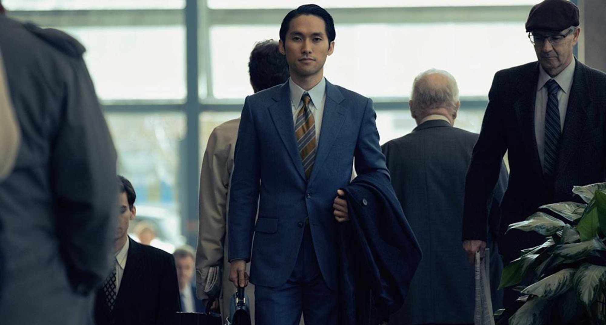 Character Solomon Baek in 'Pachinko' for Apple TV+ wearing suit in airport.