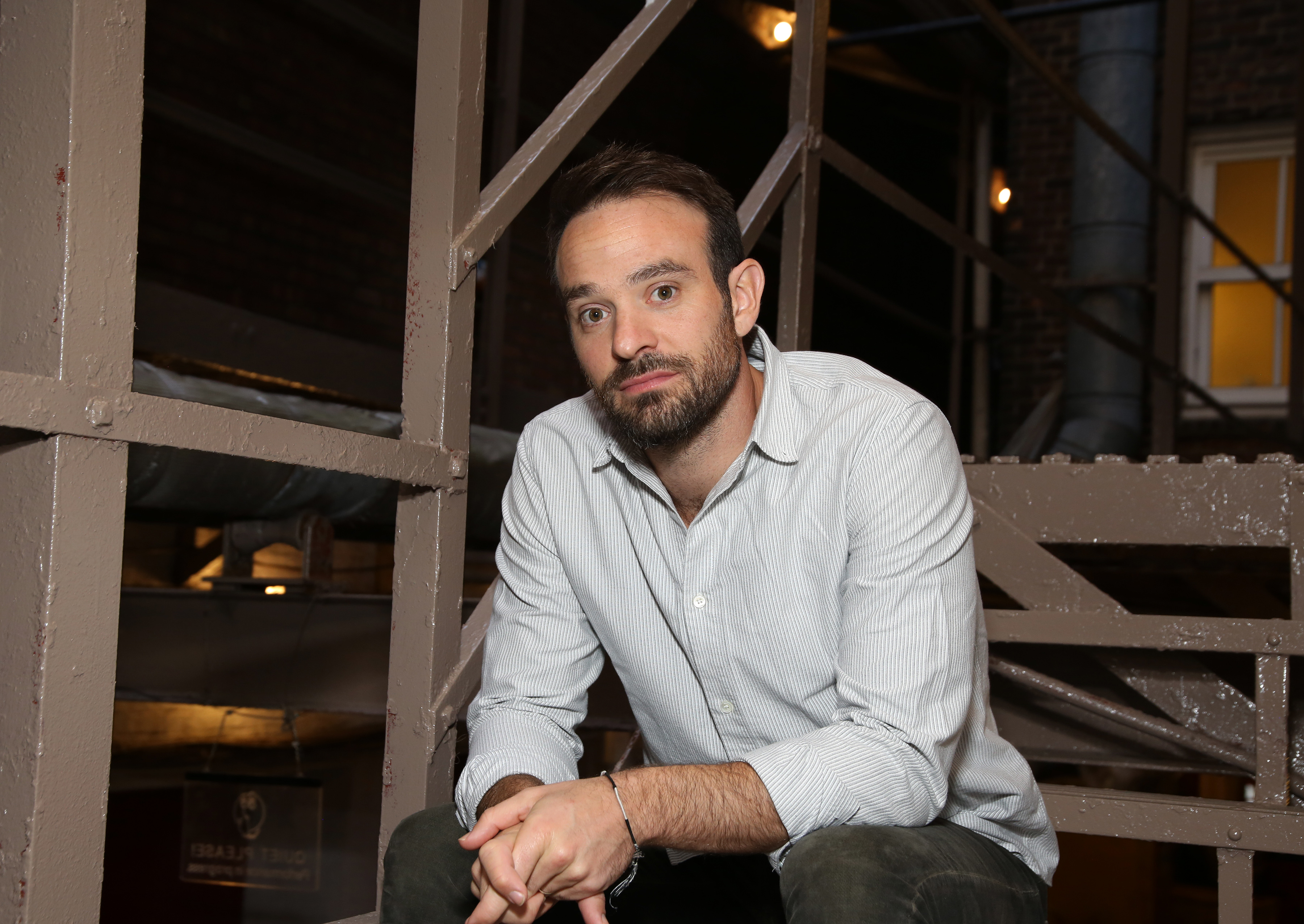 Charlie Cox, who appears as Daredevil in a 'Spider-Man: No Way Home' deleted scene, wears a white striped button-up shirt and dark gray jeans.