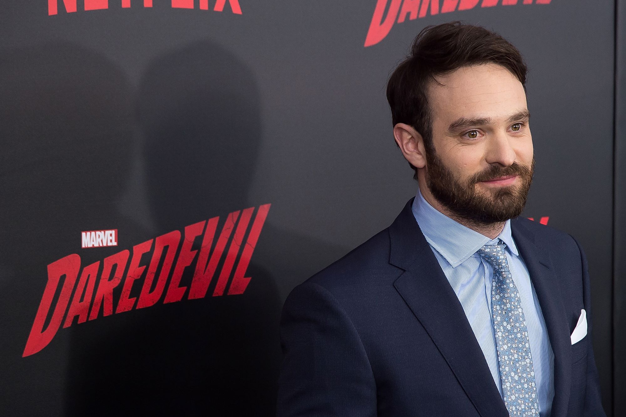 'Daredevil' star Charlie Cox wears a dark blue suit over a light blue button-up shirt and blue patterned tie.