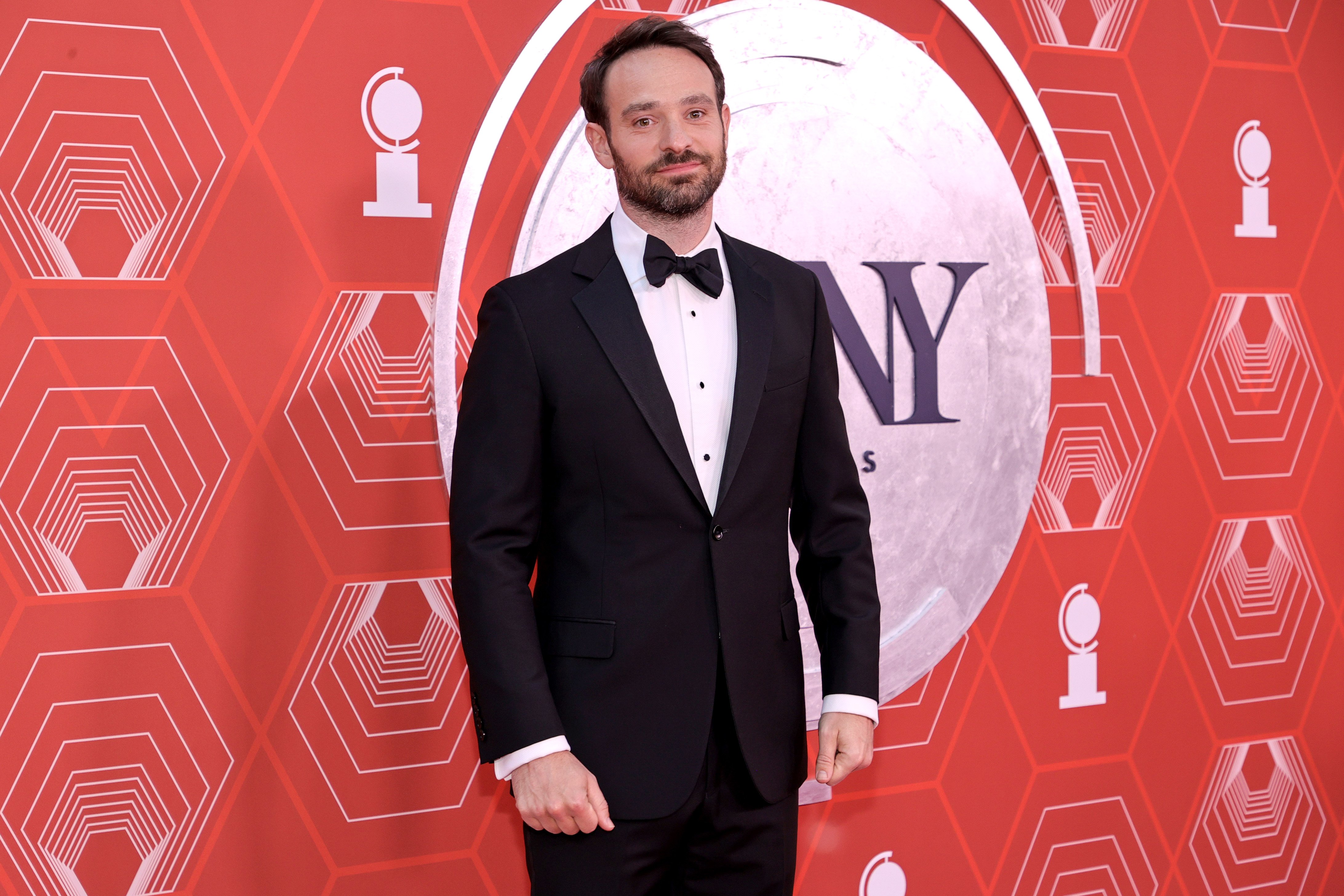 Charlie Cox, who plays Daredevil in the MCU, wears a black suit over a white button-up shirt and black bow tie.