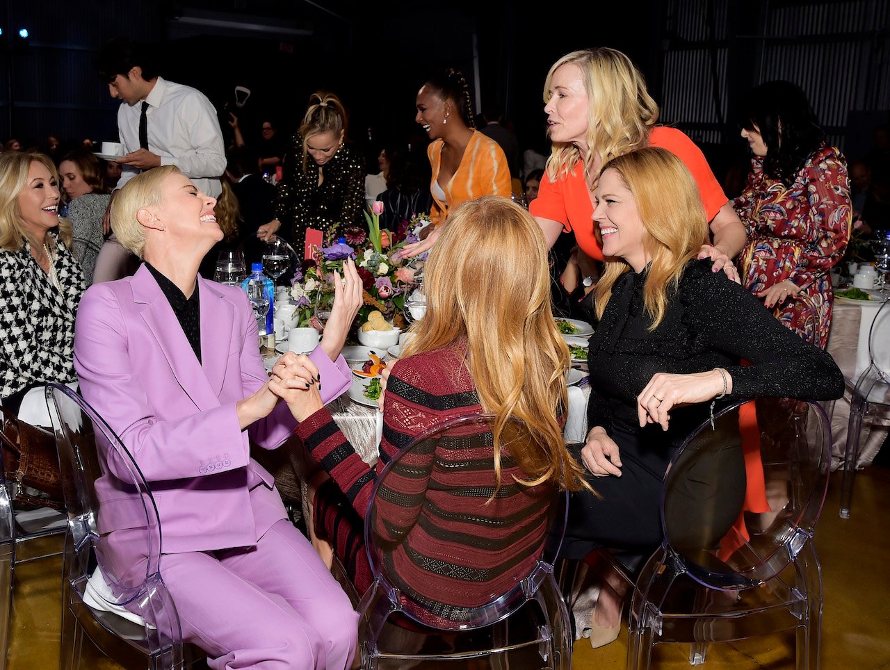Charlize Theron, Connie Britton, and Mary McCormack are seated at a table, and Chelsea Handler leans over to talk to them