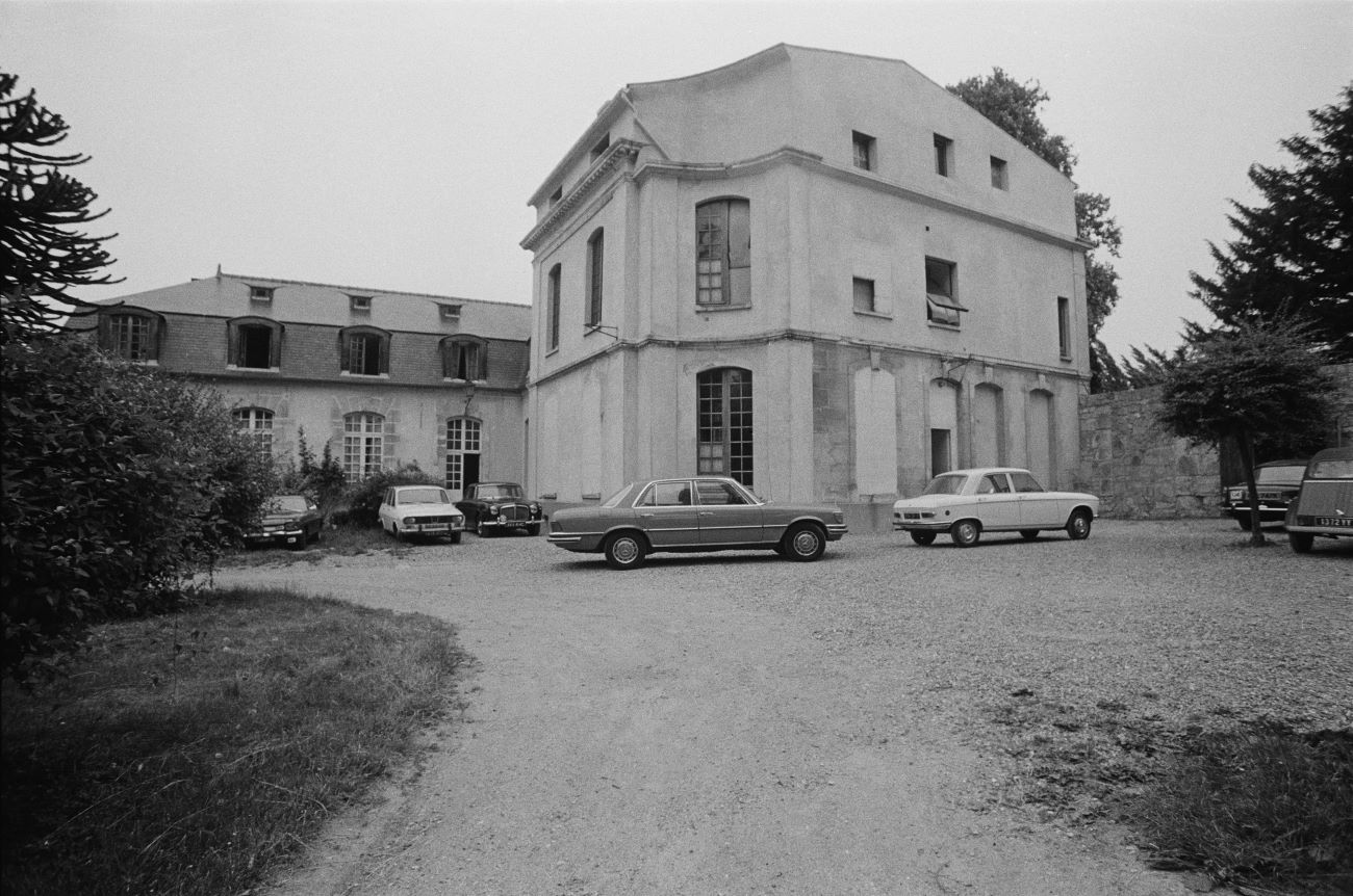 A black and white photo of Château d’Hérouville with cars parked in front of it. 