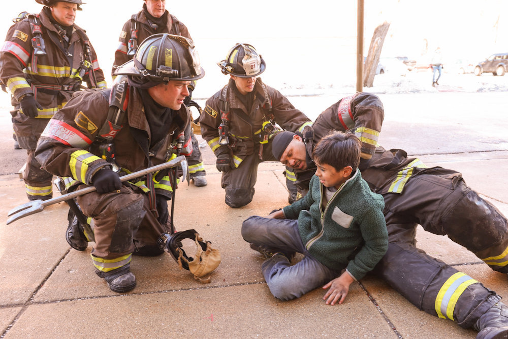 The 'Chicago Fire' Season 10 Episode 16 cast dressed in firefighting gear helping a child