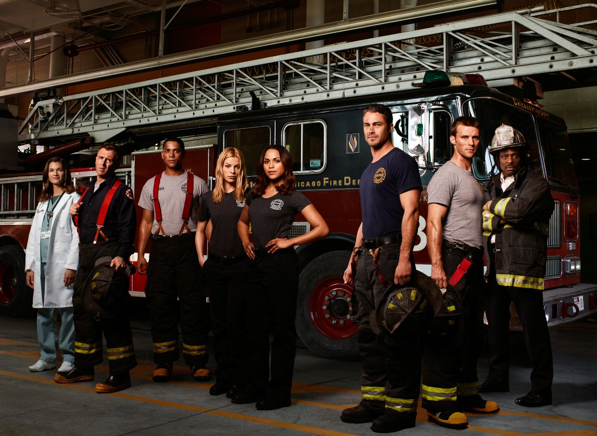 The cast of the Chicago Fire pilot stand in front of a fire truck. 