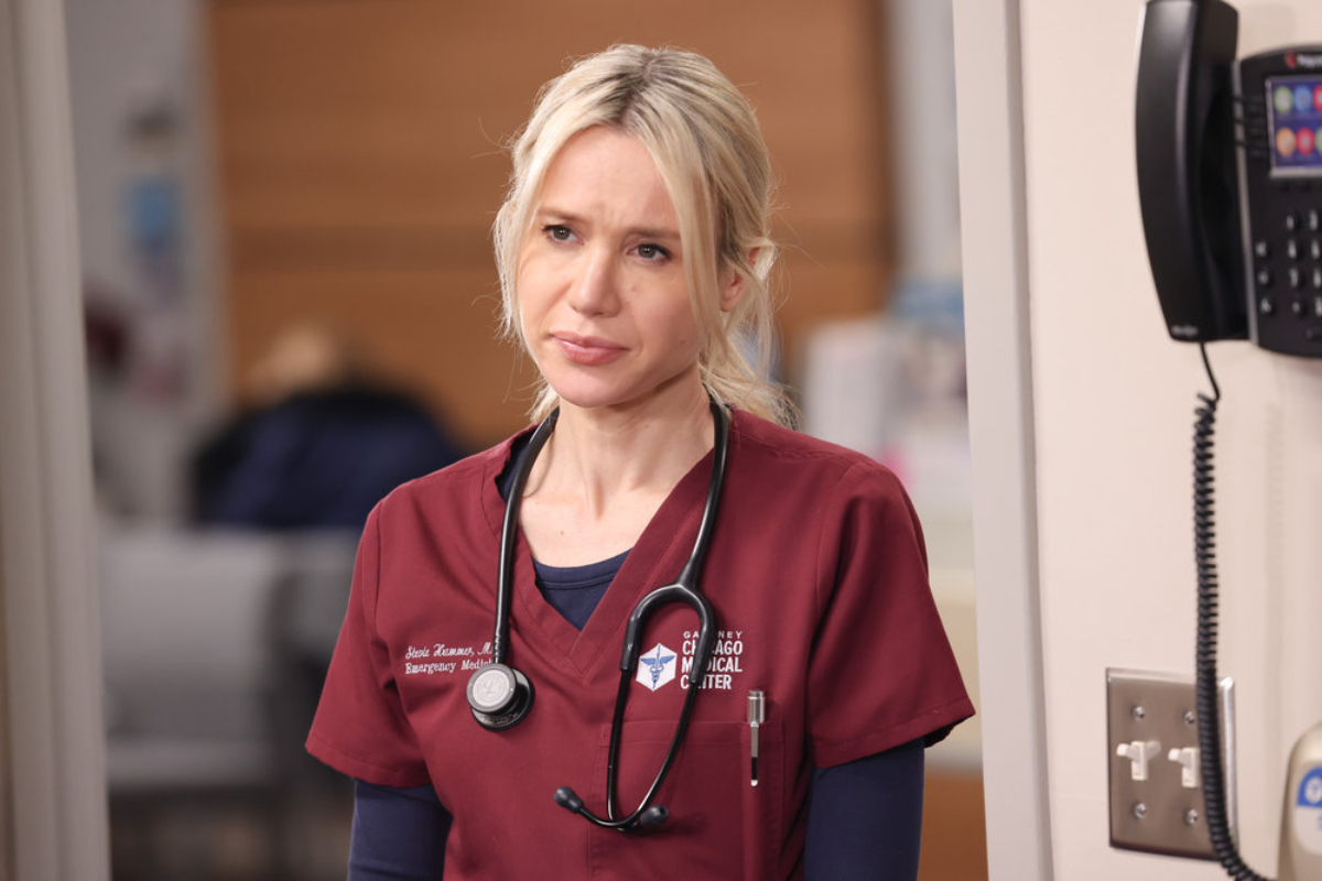 Kristen Hager as Dr. Stevie Hammer in Chicago Med Season 7. Hammer wears red scrubs and has a stethoscope around her neck.