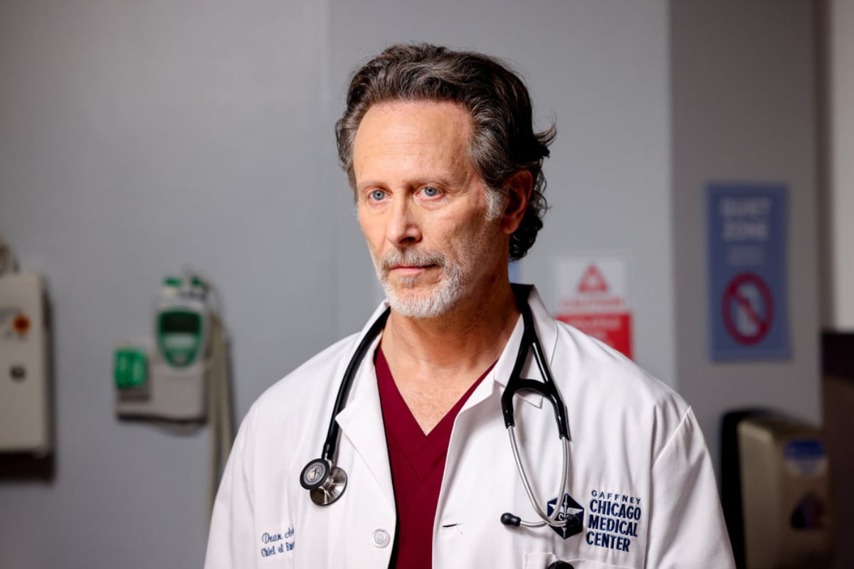 Steven Weber as Dr. Dean Archer in Chicago Med. Dr. Archer wears maroon scrubs, a white lab coat, and a stethoscope around his neck.
