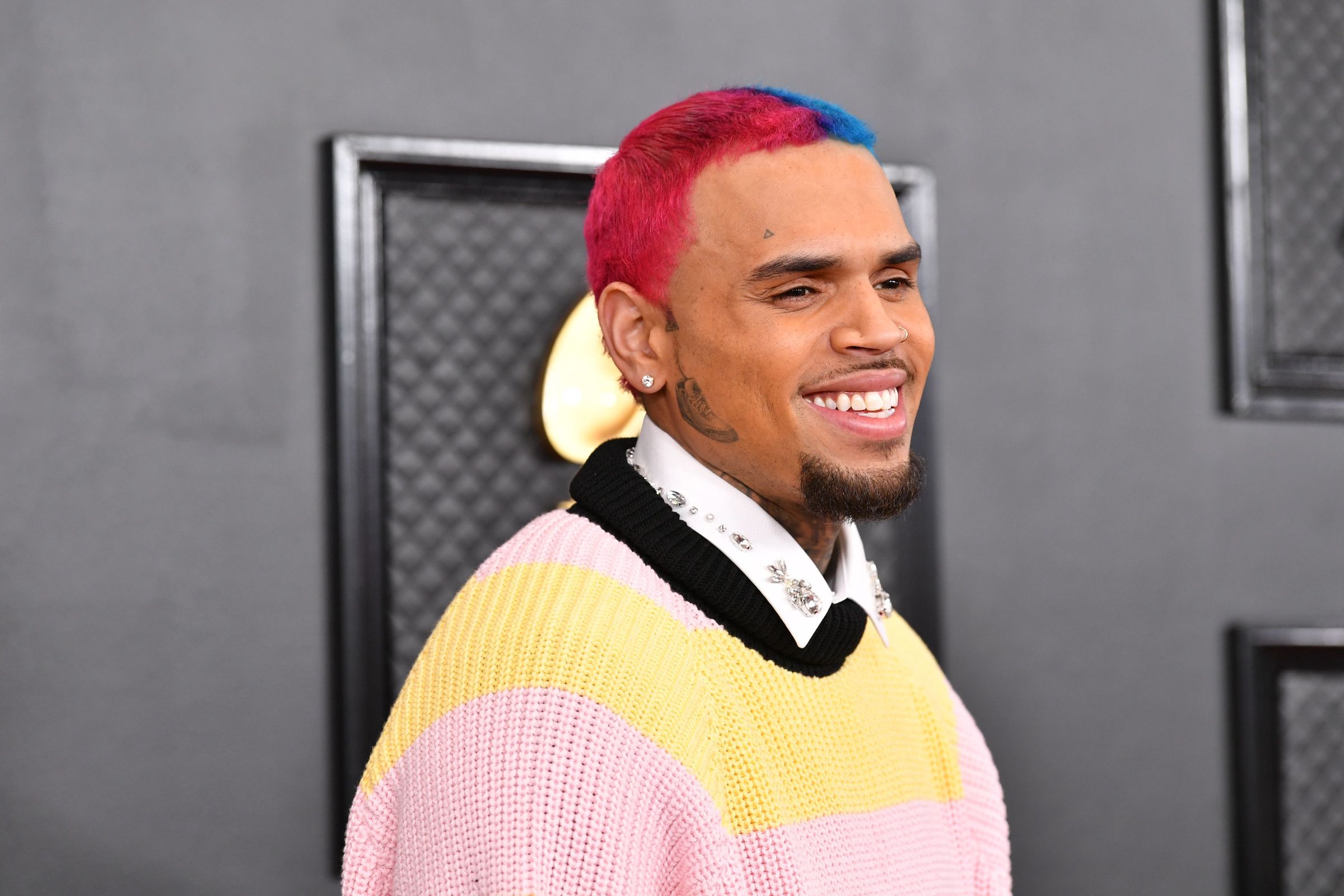 Chris Brown smiling wearing a yellow and pink jacket