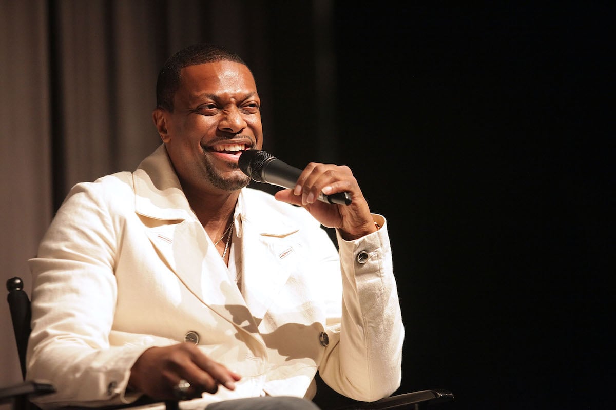 Chris Tucker wears a white suit and laughs into microphone