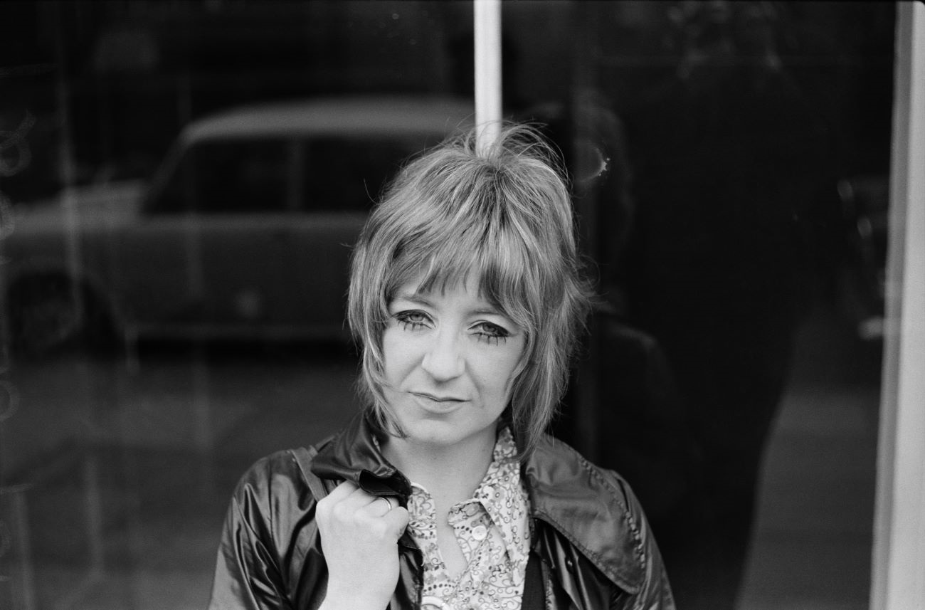 A black and white photo of Christine McVie wearing a jacket and patterned shirt. She joined Fleetwood Mac several years later.