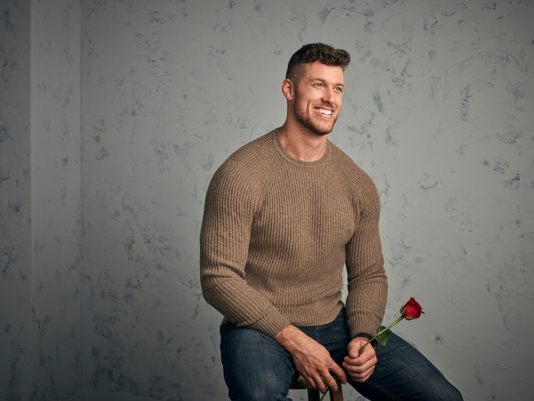 Clayton Echard, 'The Bachelor,' smiling while sitting down and holding a rose