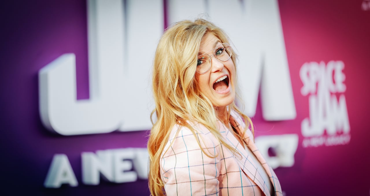 Connie Britton in a pink plaid jacket and gold glasses, her mouth wide open in a smile