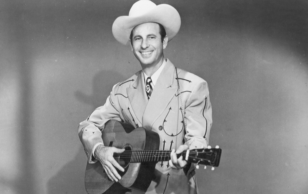 Cowboy Copas in a suit and cowboy hat, holding a guitar and smiling