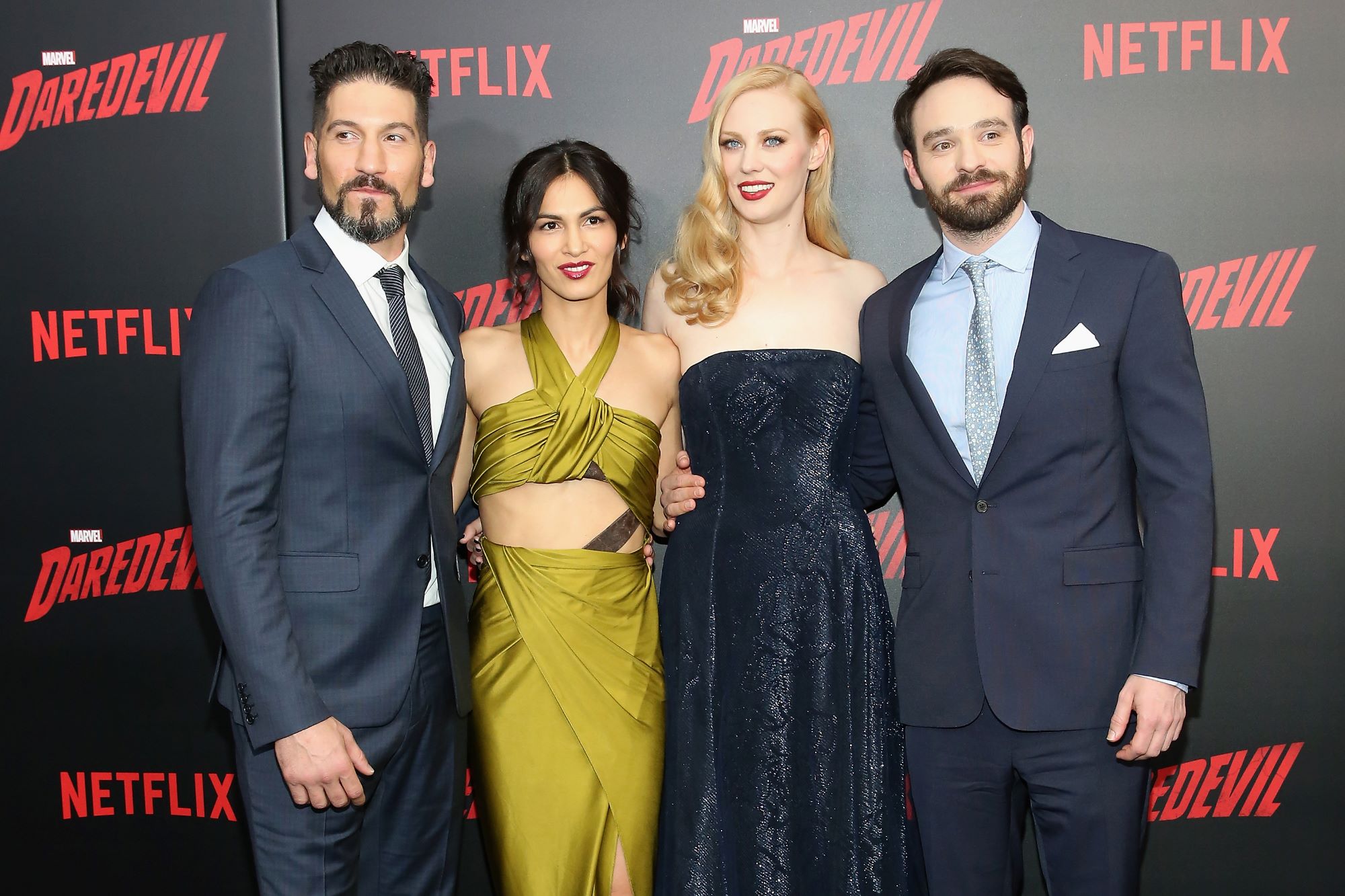 Jon Bernthal, Elodie Yung, Deborah Ann Woll, and Charlie Cox, who fans want to see in 'Daredevil' Season 4, pose for pictures. Bernthal wears a dark blue suit over a white button-up shirt and black striped tie. Yung wears a olive green dress. Woll wears a dark blue sparkly strapless dress. Cox wears a dark blue suit over a light blue button-up shirt and light blue tie.