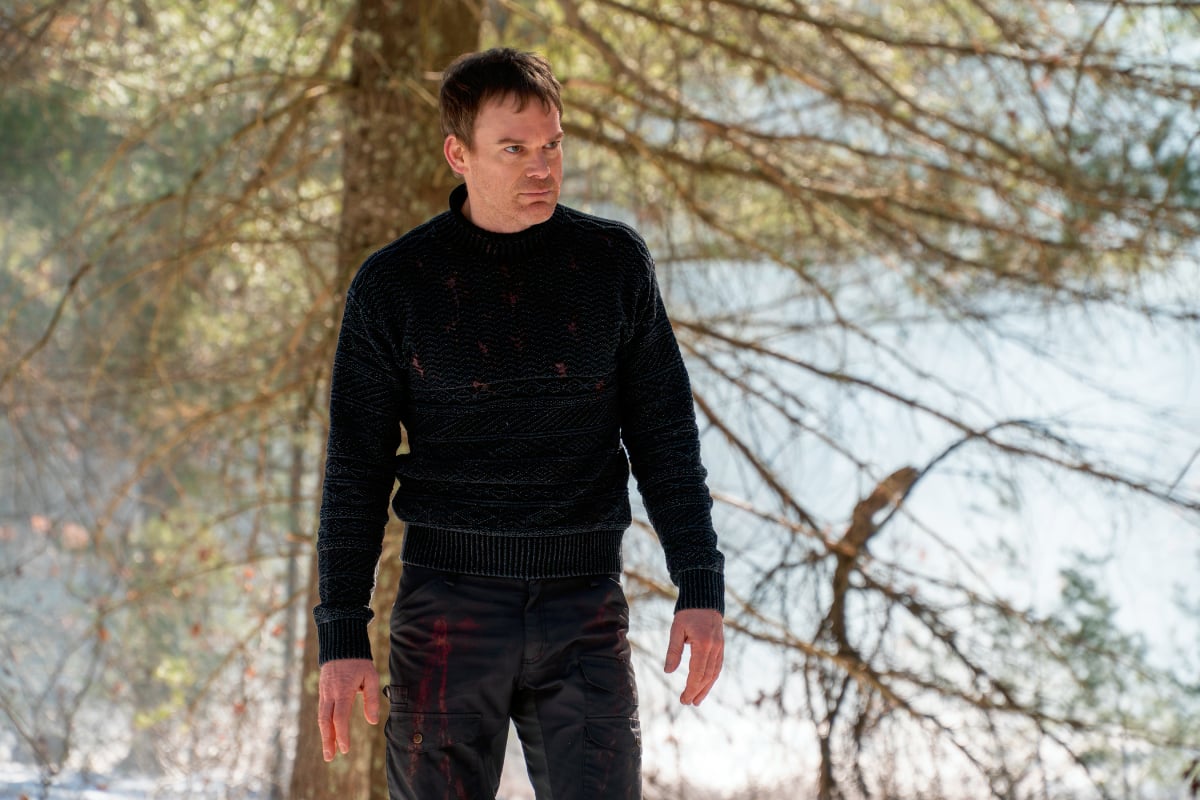 Michael C. Hall as Dexter in Dexter: New Blood. Dexter stands in the woods wearing a sweater.