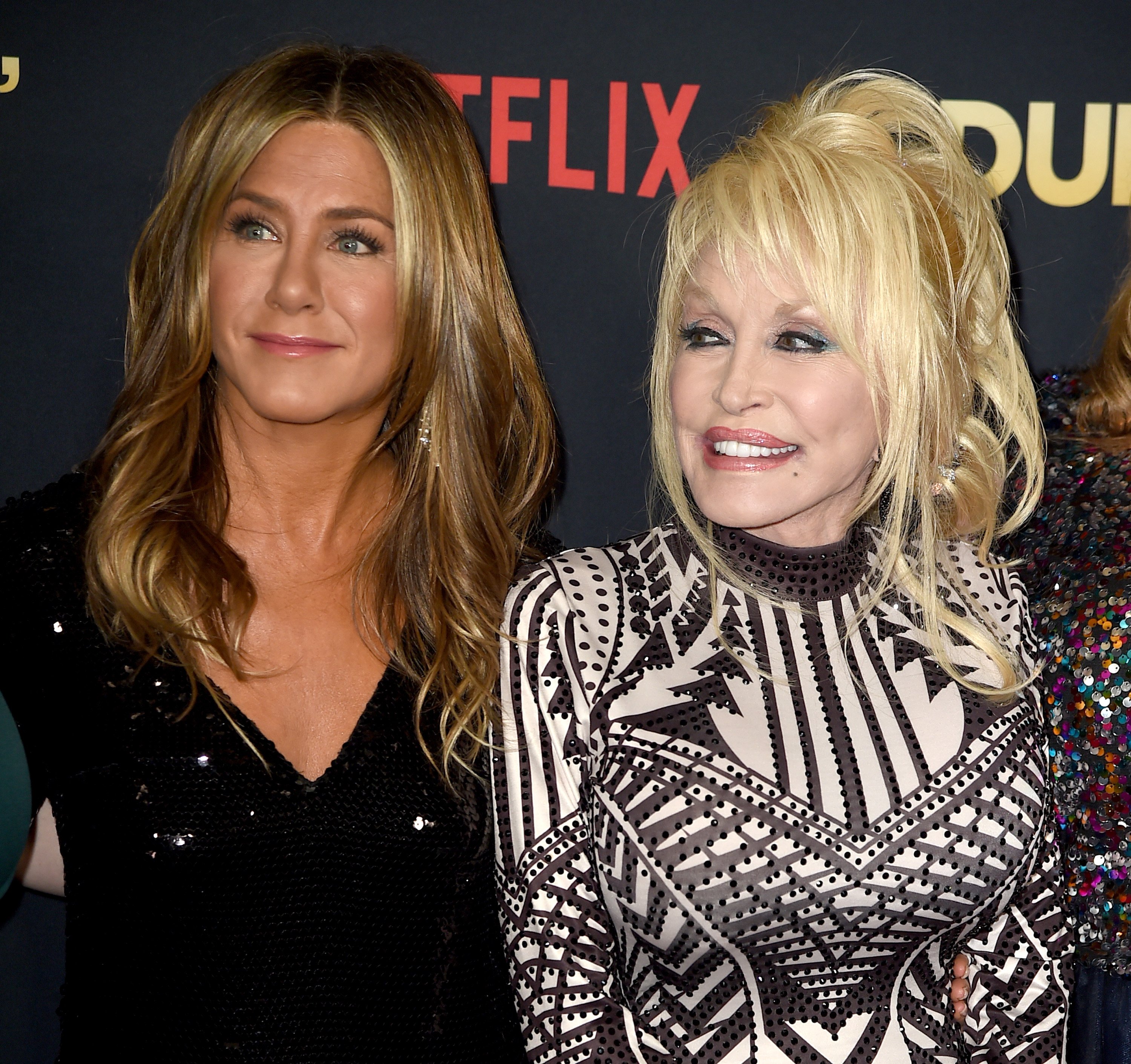 Jennifer Aniston wears a black sparkly shirt and Dolly Parton wears a black and white patterned shirt.