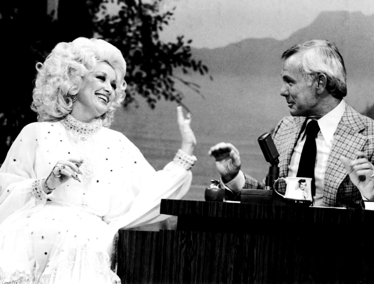 Black and white photo of Dolly Parton laughing and reaching towards Johnny Carson on 'The Tonight Show'