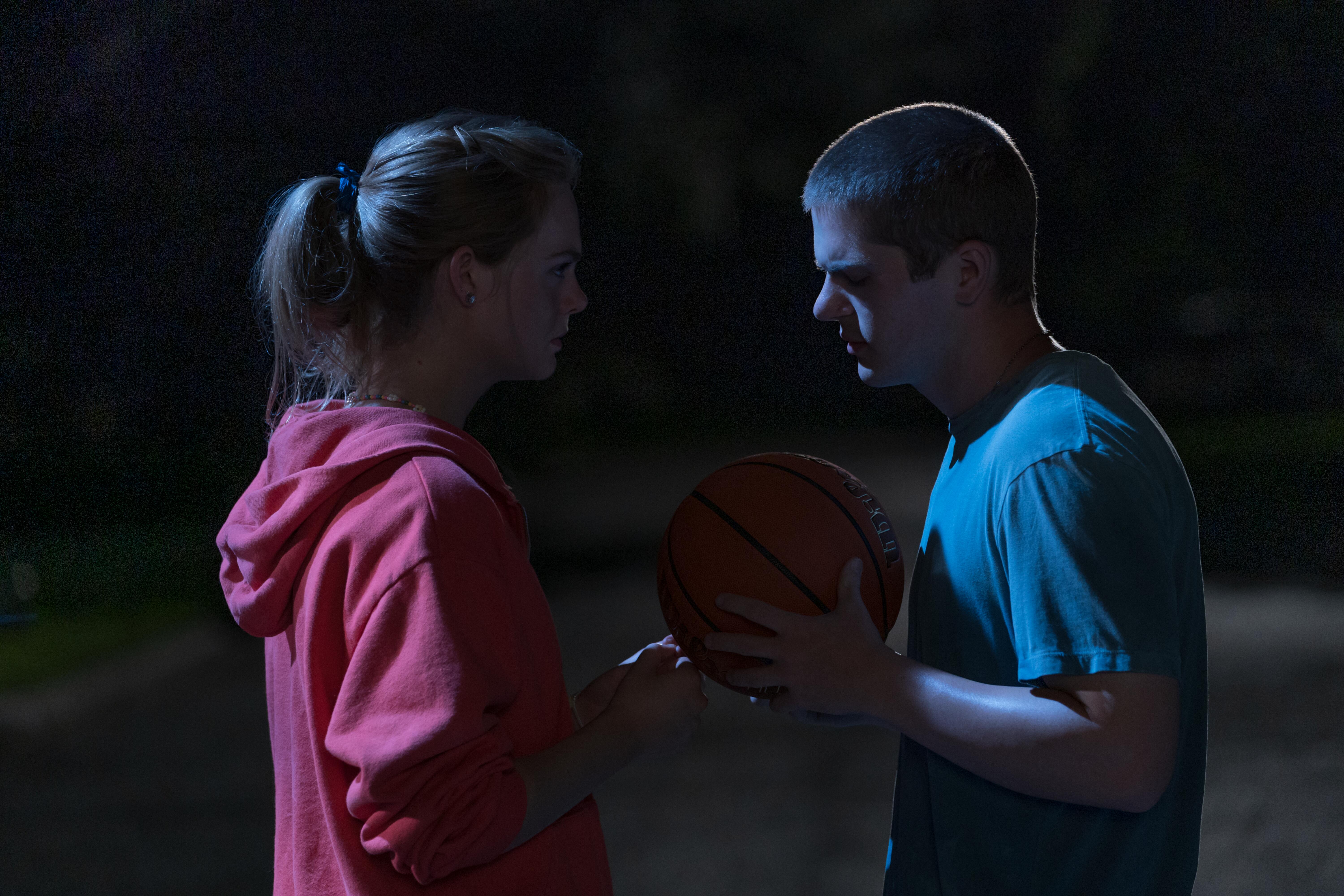 Elle Fanning and Colton Ryan standing across from each other with the latter holding a basketball