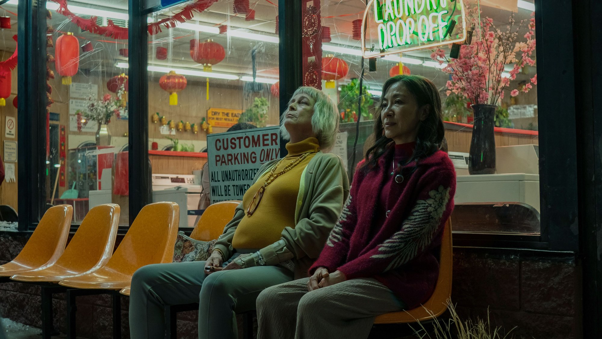 'Everything, Everywhere All at Once' Jamie Lee Curtis as Deirdre Beaubeirdra and Michelle Yeoh as Evelyn Wang sitting next to each other in front of the laundromat