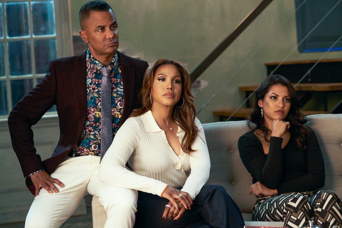 Toni Braxton and Humberly González sitting on a couch with Yanic Truesdale standing behind them in the Lifetime movie 'Fallen Angels Murder Club: Friends to Die For'
