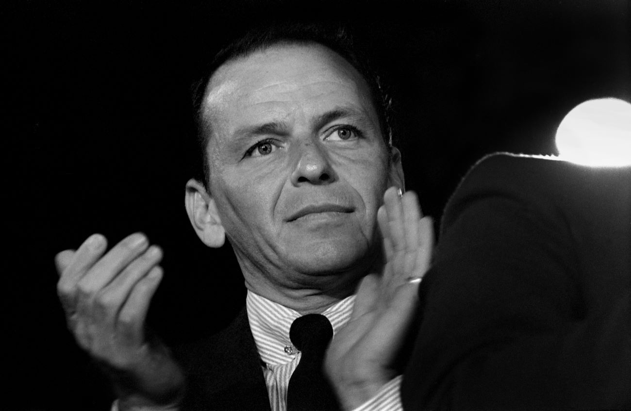 A black and white picture of Frank Sinatra wearing a tie and clapping his hands. 