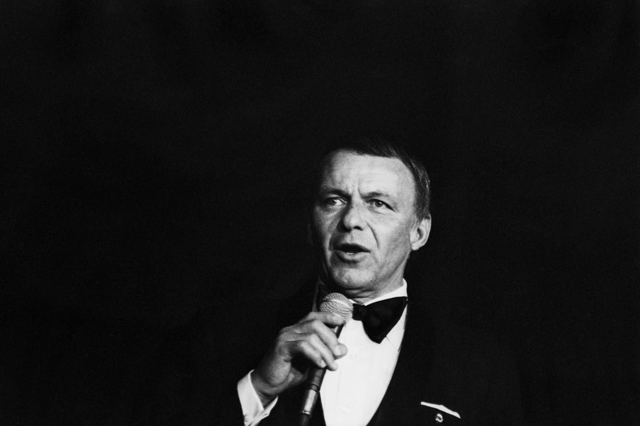 A black and white photo of Frank Sinatra wearing a tuxedo and holding a microphone.