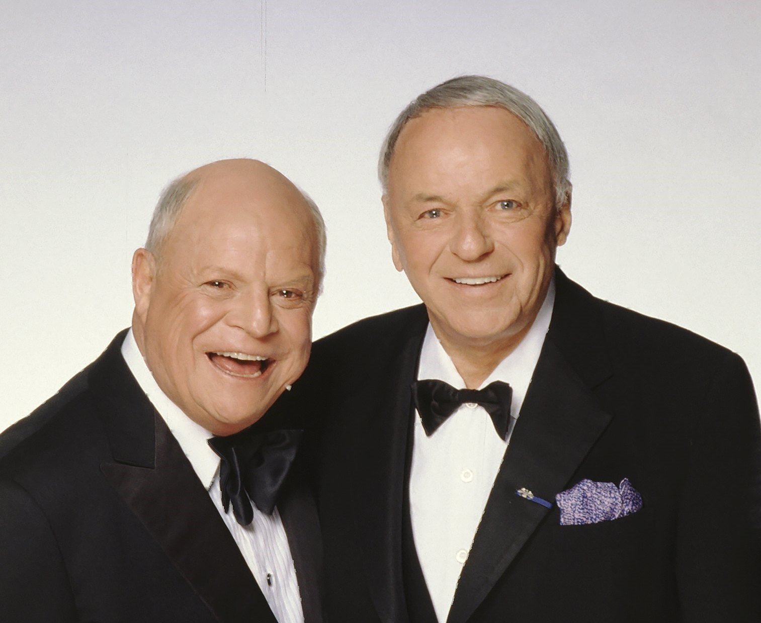 Don Rickles and Frank Sinatra wear tuxedos and stand in front of a white background.