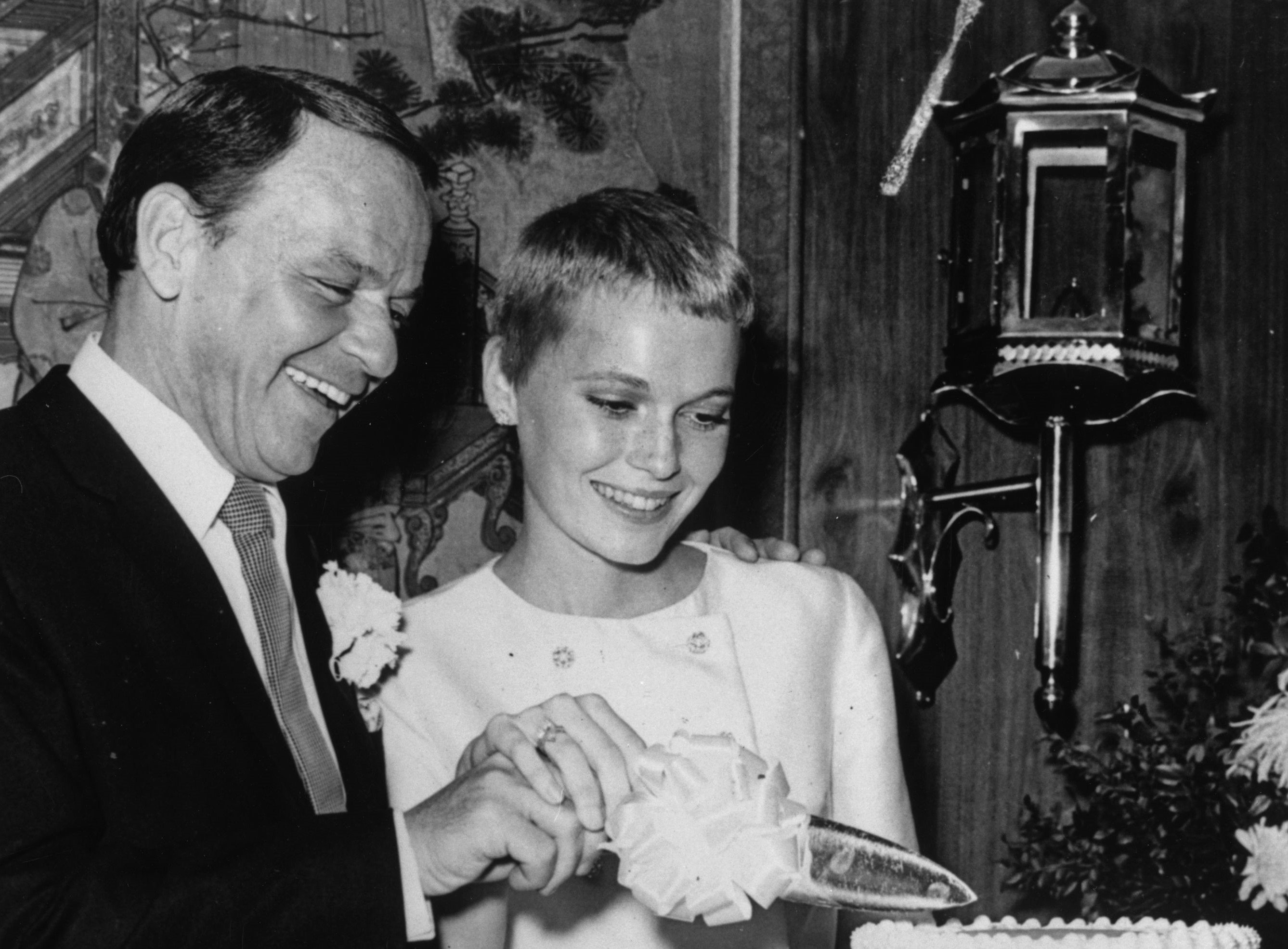A black and white photo of Frank Sinatra and Mia Farrow cutting a cake together.