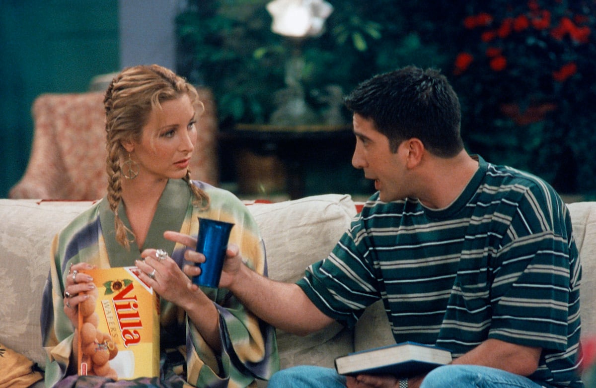 Lisa Kudrow as Phoebe Buffay and David Schwimmer as Ross Geller sit on a couch while filming 'Friends' in 1996
