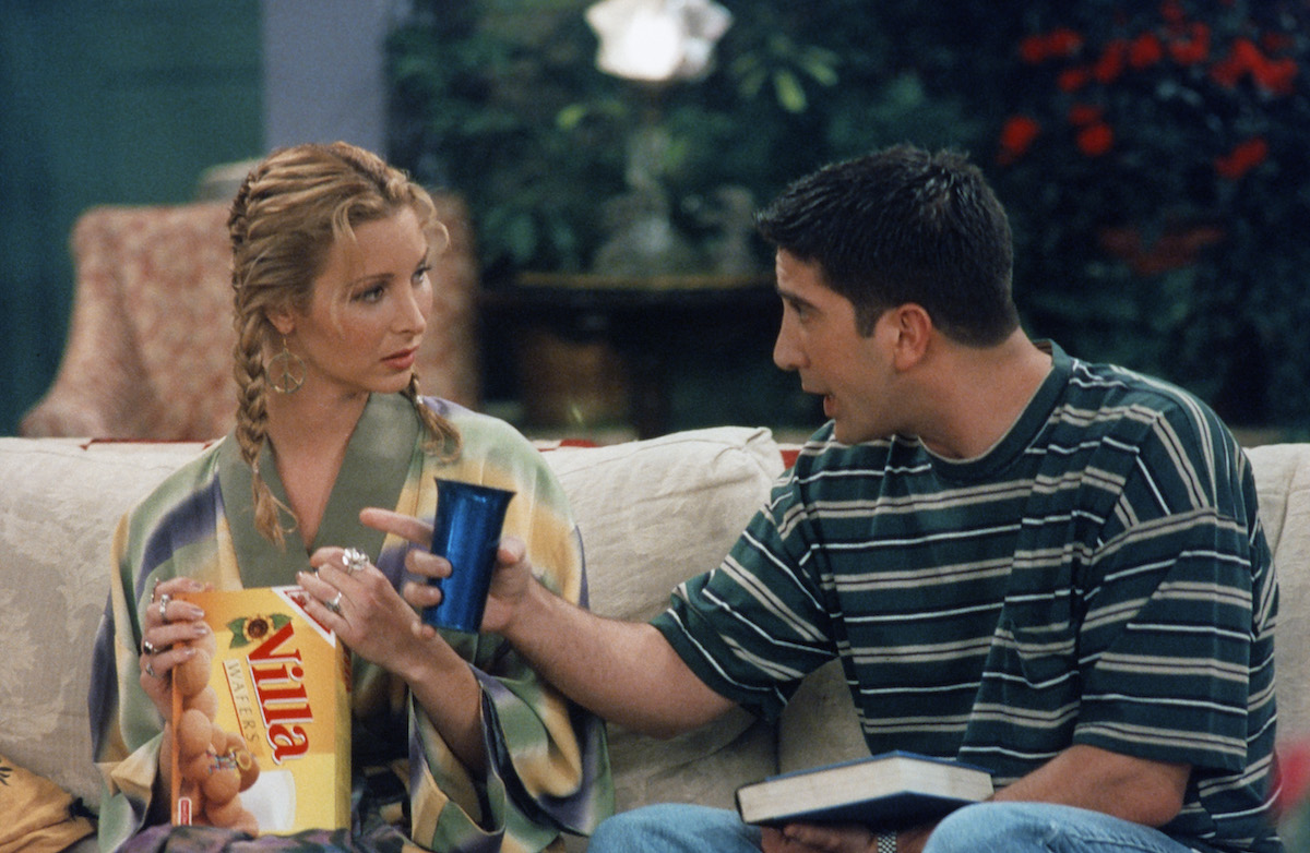 Lisa Kudrow as Phoebe Buffay and David Schwimmer as Ross Geller sit on a couch while filming 'Friends' in 1996