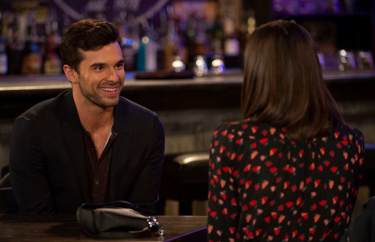 Josh Swickard smiling while talking to a female cast member during a scene on 'General Hospital'