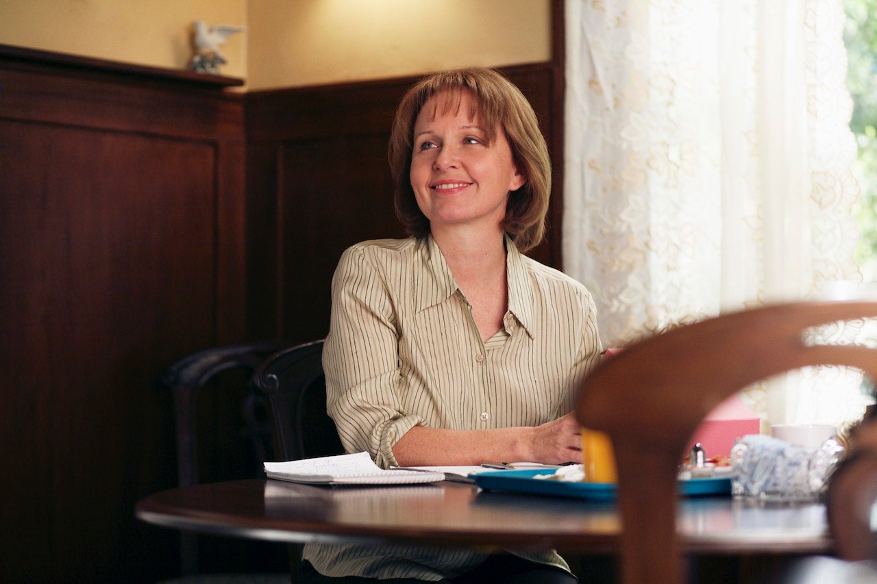 Kate Burton as Ellis Grey in 'Grey's Anatomy' sits at a table smiling.