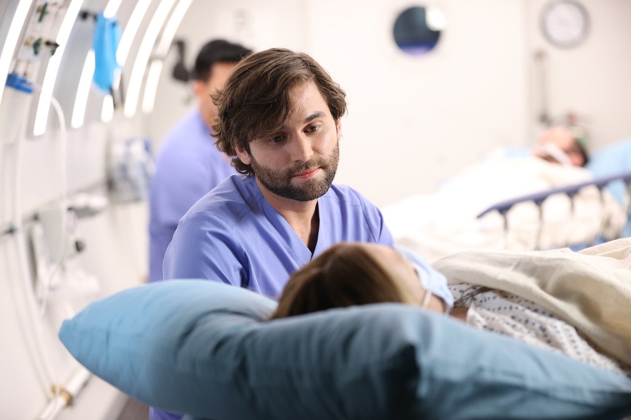 Jake Borelli as Levi Schmitt on 'Grey's Anatomy' talks to a patient in blue scrubs.