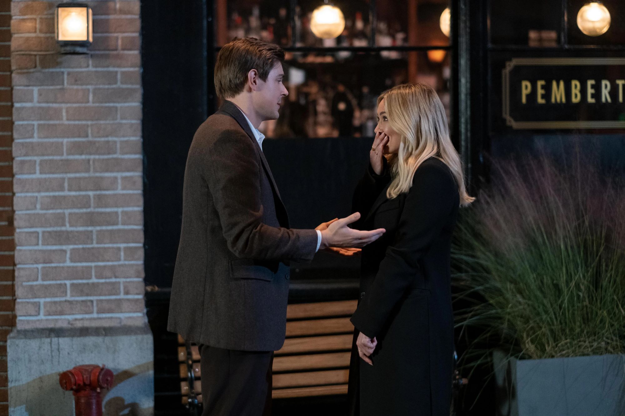 'How I Met Your Father' Season 1 Episode 9 stars Chris Lowell and Hilary Duff, in character as Jesse and Sophie, share a scene. Jesse wears a dark brown suit. Sophie wears a black coat.