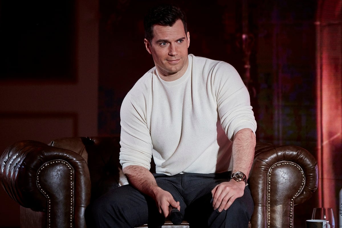 Henry Cavill smirking while wearing a white sweater.