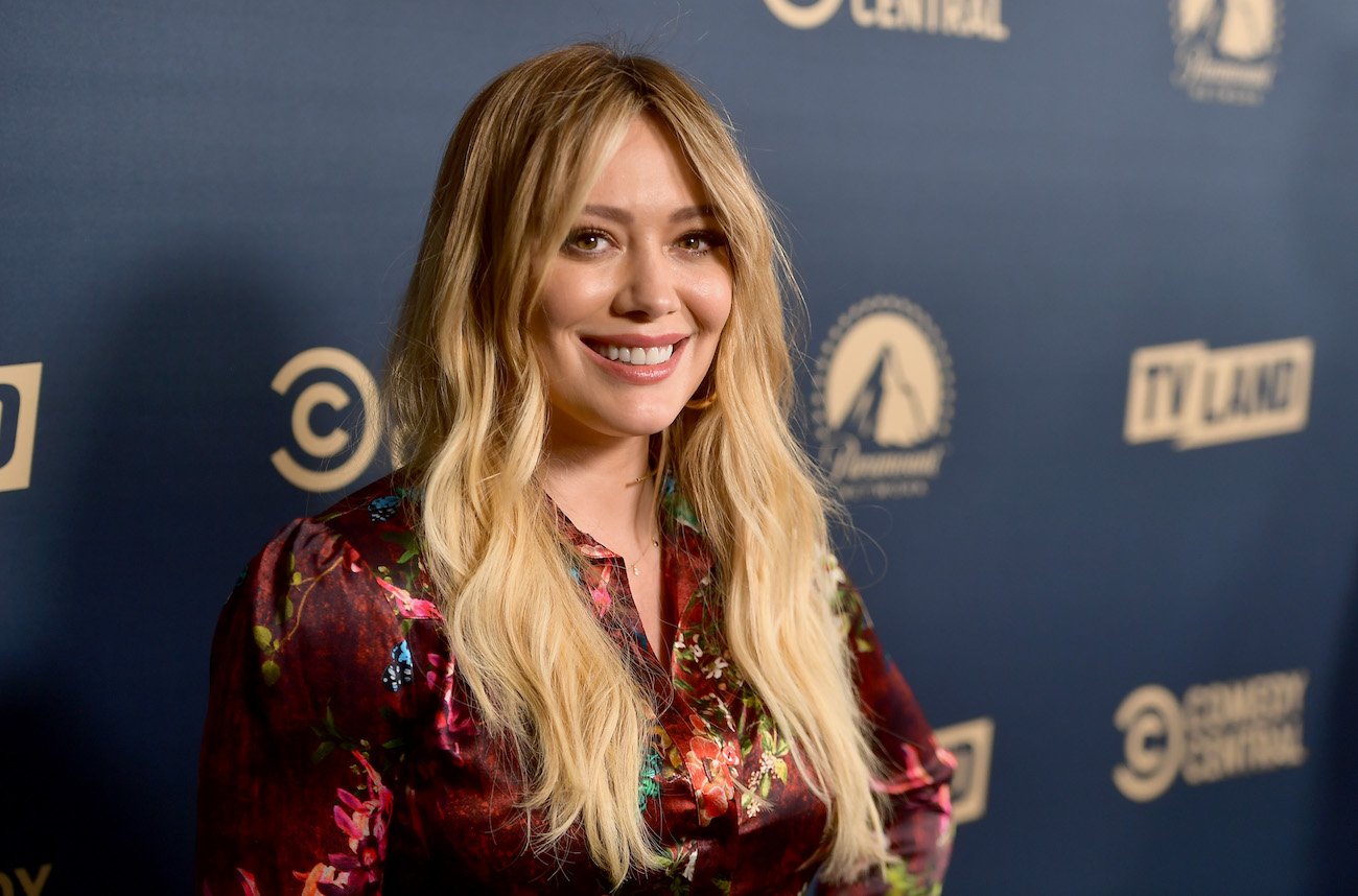 Hilary Duff smiling at the camera while having long blonde hair and wearing a red outfit