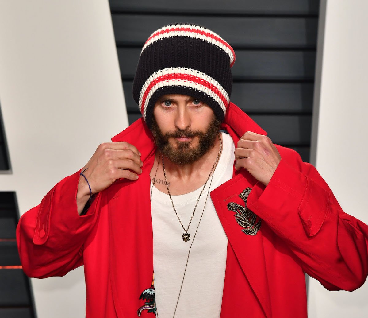 Jared Leto poses in a hat and red jacket