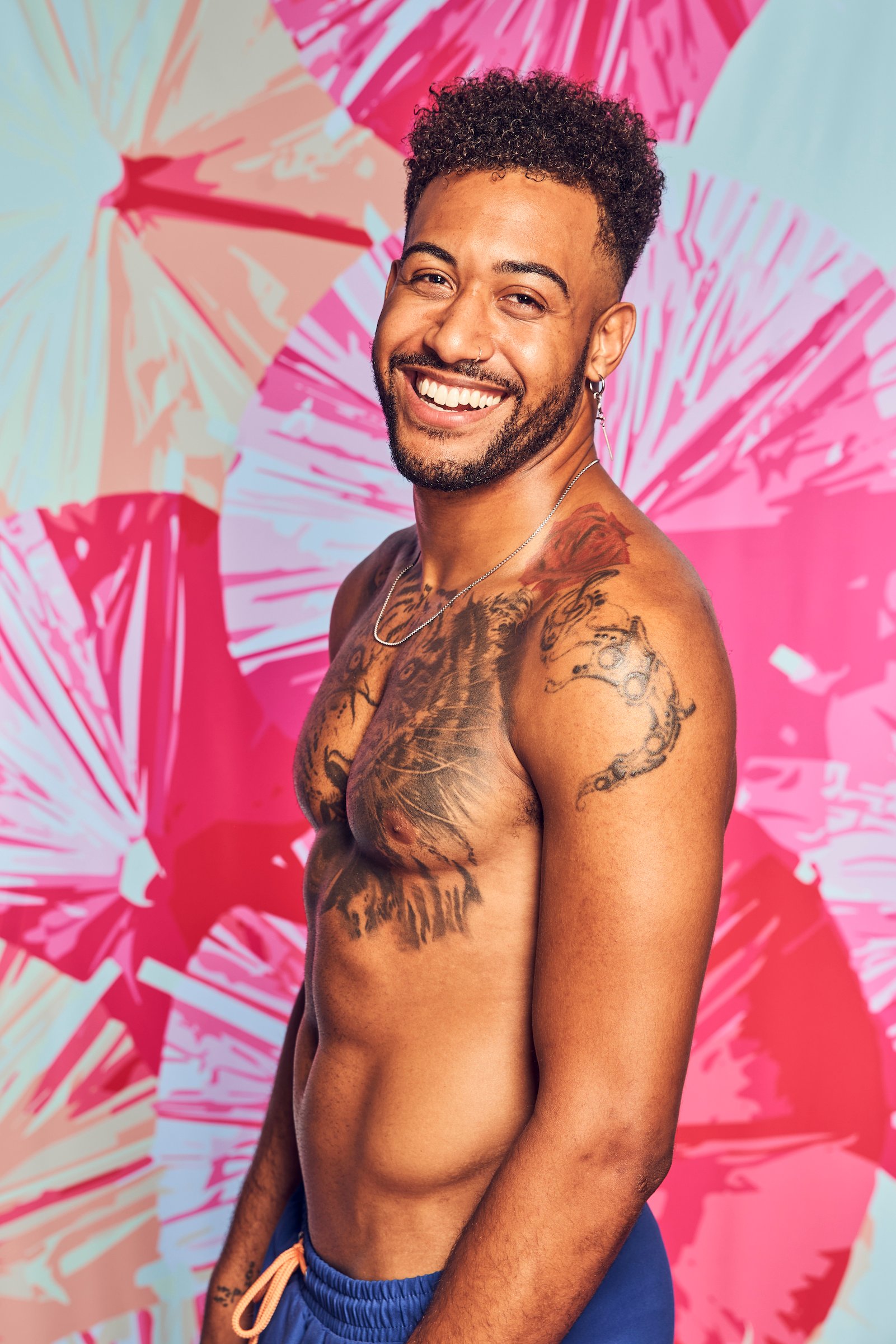 Javonny Vega, a contestant on CBS 'The Challenge,' smiling and shirtless against a pink background
