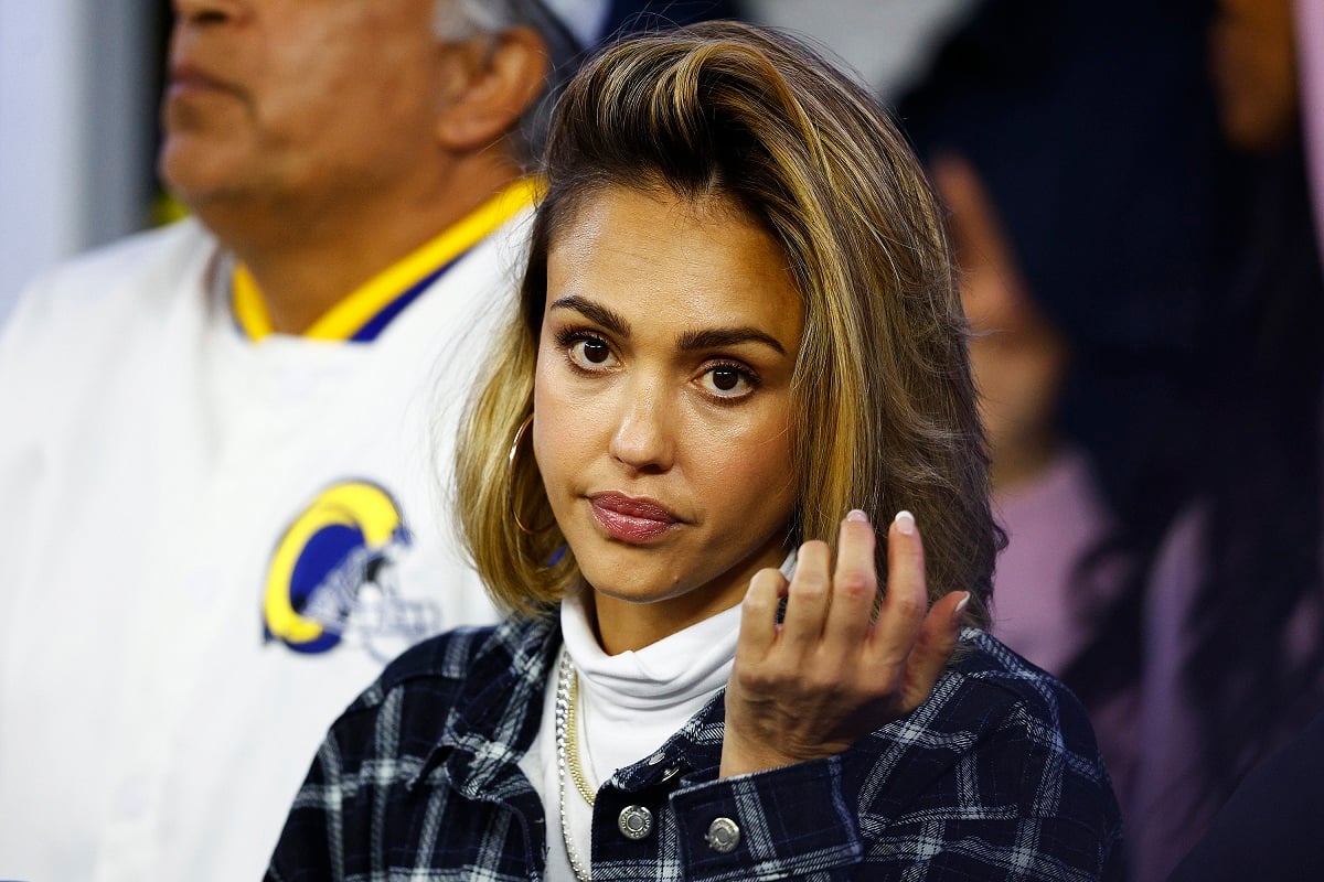 Jessica Alba sitting down while wearing a brown jacket.