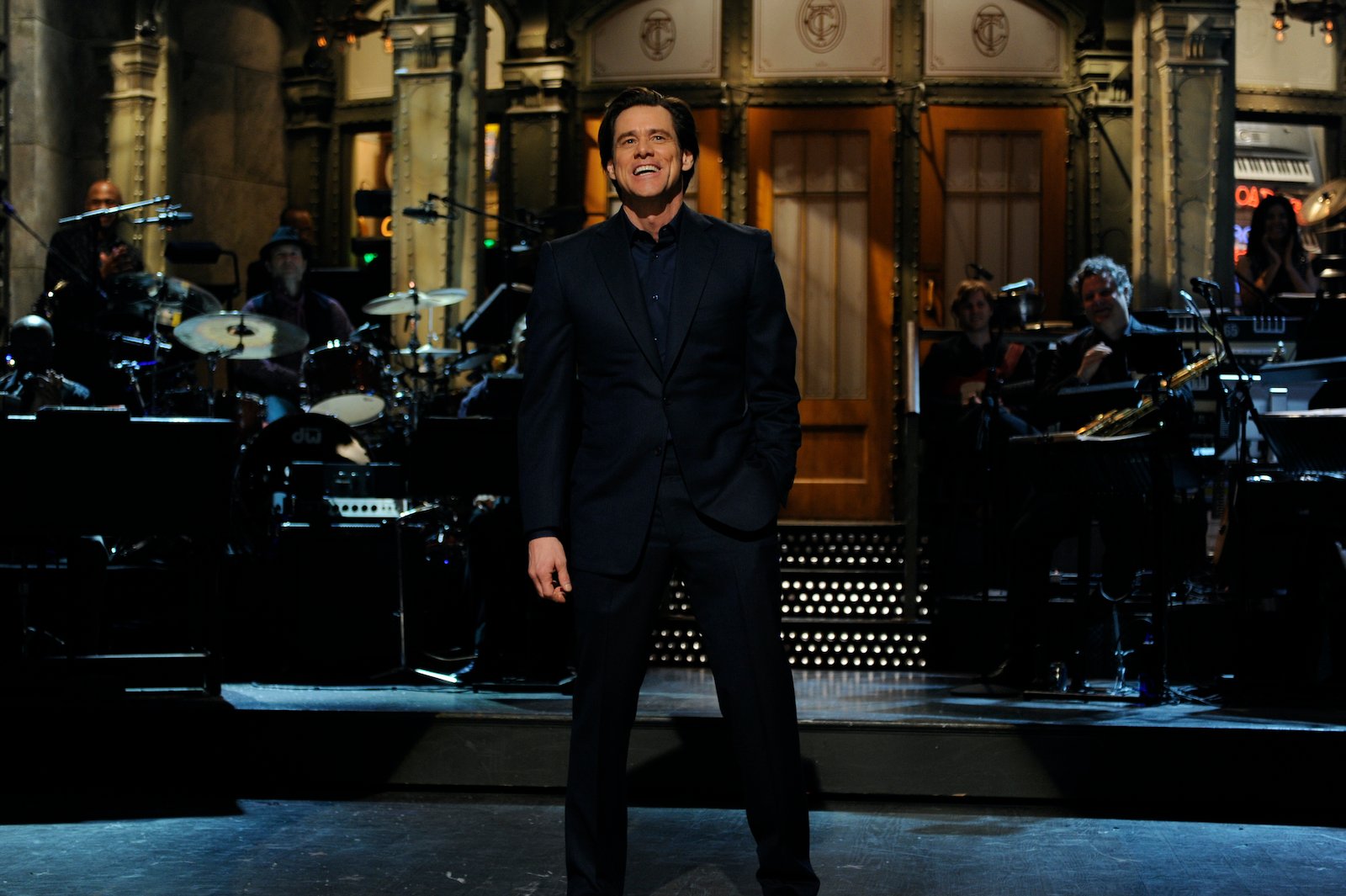 Jim Carrey hosting SNL, smiling and wearing a black suit on stage.