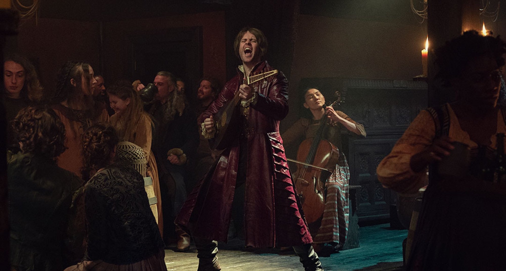 Joey Batey as Jaskier in 'The Witcher' Season 2 singing on table.