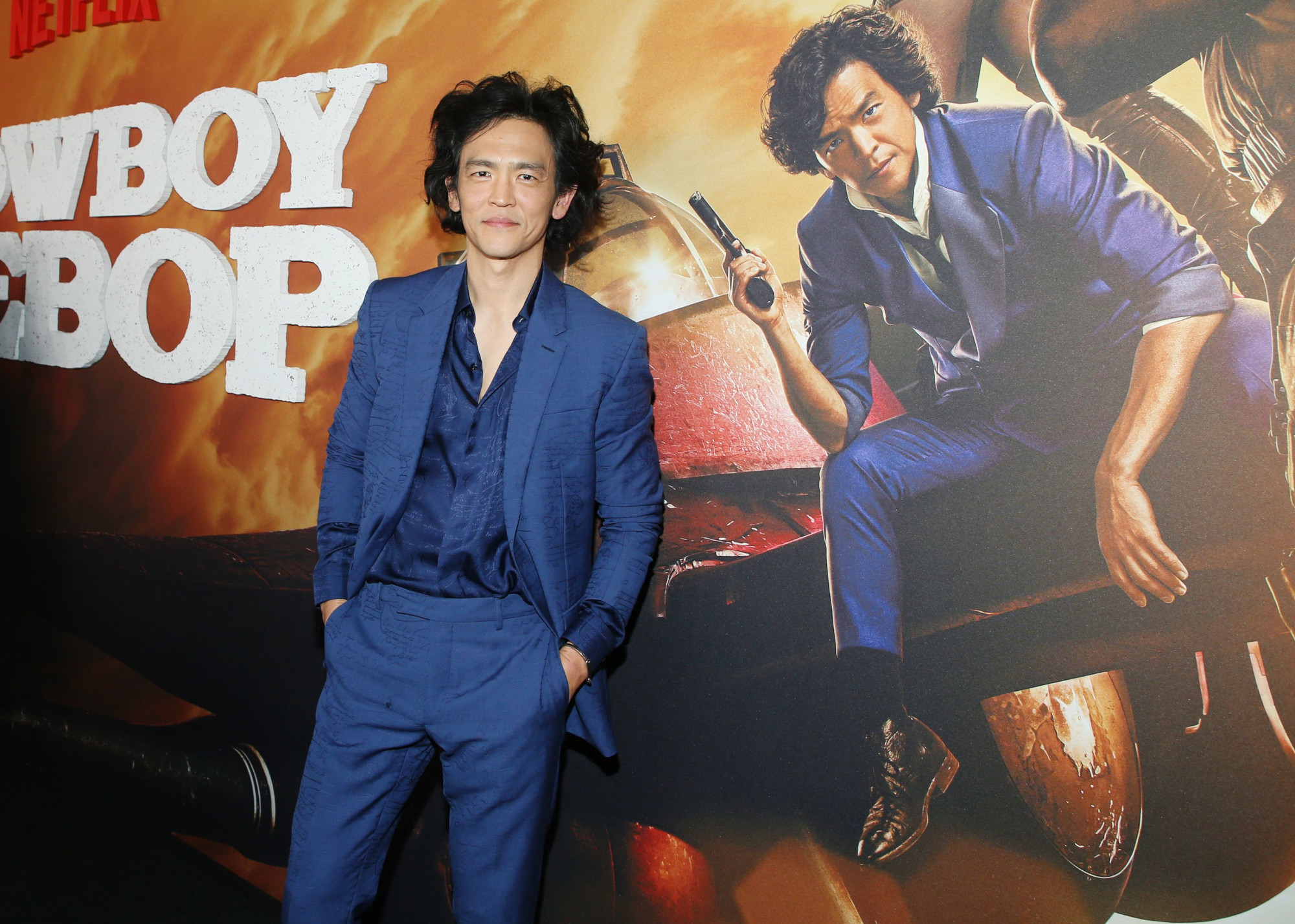 John Cho at the premiere for Netflix's live-action 'Cowboy Bebop.' He's wearing a blue suit and standing in front of an image promoting the series.