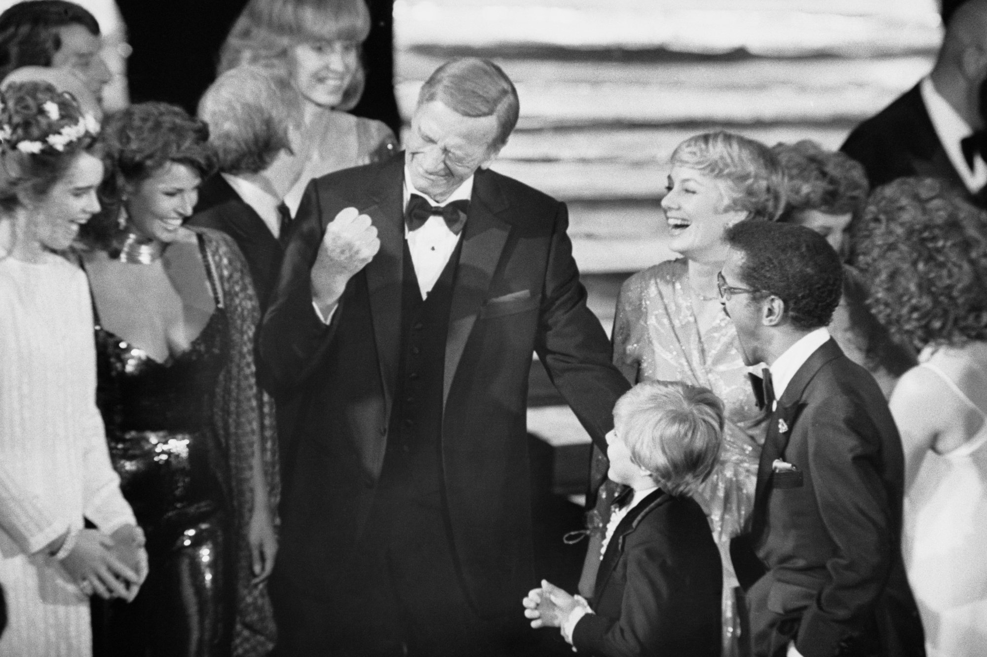 John Wayne 1979 Oscars Rick Schroder, Shirley Jones, Sammy Davis, Jr., Brooke Shields, Racquel Welch, Yul Brynner and David L. Wolper in formal clothes smiling at each other