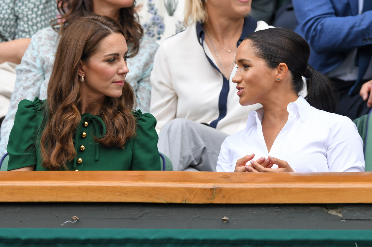 Kate Middleton and Meghan Markle talking to each other at a sports game